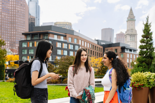 Three Simmons students talking in the Academic quad, with a view of some of Boston's tall buildings in the background